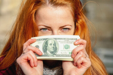 Beautiful business woman holds money as symbol of best motivation for work. Selective focus on eyes.