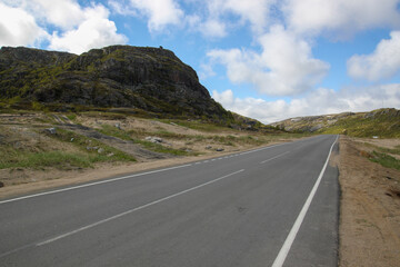 A asphalt road between the hills. The path that goes beyond the horizon. White clouds on a blue sky. Rural landscape.