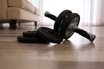 Fototapeta na wymiar Abs roller and weight plates on floor in room. Home fitness