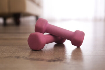 Pink dumbbells on floor in room, closeup. Home fitness