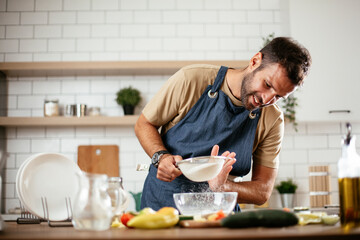 Fototapeta na wymiar Attractive man cooking in modern kitchen. Handsome man playing with flour while preparing delicious food.