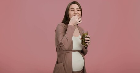 Studio portrait of young pregnant lady enjoying pickles, eating them from jar, pink background - Powered by Adobe