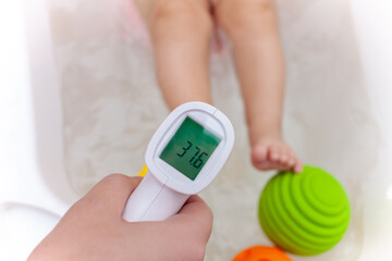 Comfortable water temperature in the bathroom. female hand with infrared thermometer