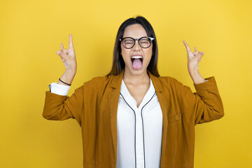 Young beautiful woman wearing a blazer over isolated yellow background shouting with crazy expression doing rock symbol with hands up