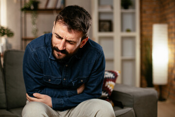 Fototapeta premium Sick man at home. Young man sitting on sofa having fever.