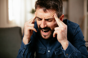 Sick man at home. Young man sitting on sofa having fever.