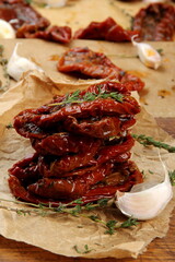 Sun dried tomatoes, dried tomato halves with thyme, garlic on olive oil on baked paper, top view