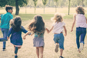 Group of kids running on grass together, having race in park. Back view, full length. Children outdoor activity concept