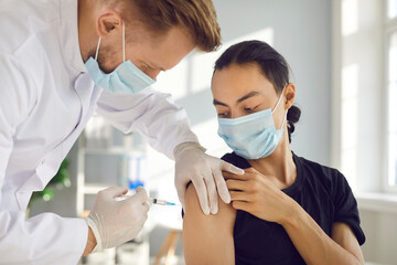 Young man in medical face mask getting flu shot during seasonal infection outbreak. Male doctor or nurse giving effective Covid-19 vaccine injection to patient during modern vaccination campaign - obrazy, fototapety, plakaty