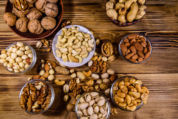 Various nuts (almond, cashew, hazelnut, pistachio, walnut) in bowls on a wooden table. Vegetarian meal. Healthy eating concept. Top view