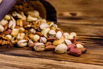 Various nuts (almond, cashew, hazelnut, pistachio, walnut) scattered from bag on a wooden table. Vegetarian meal. Healthy eating concept