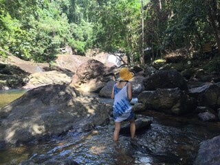 A woman in a yellow hat is climbing a rock in the middle of the river.