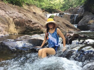 A woman in a yellow hat is climbing a rock in the middle of the river.