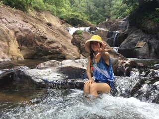A woman in a yellow hat is climbing a rock in the middle of the river.