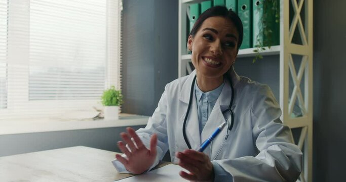 Emotional smiling medical worker chatting amicably at workplace, gesturing actively with hands, giving explanation.