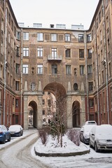 an old building with three high arches in winter. there are cars in the yard and there is snow