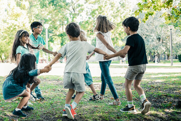 Happy children playing together outdoors, dancing around on grass, enjoying outdoor activities and...