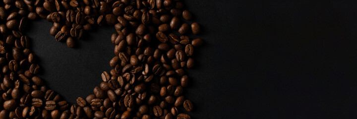 Banner with fresh roasted coffee beans closeup on black stone background. Place for text in the shape of a heart. Top view, flat lay with copy space