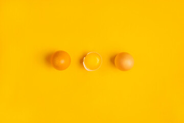 Three farm brown chicken eggs with one yolk on yellow table. Minimalistic product concept. Healthy food or Happy Easter concept. Top view, flat lay