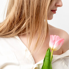 Obraz na płótnie Canvas Half face portrait of a beautiful young caucasian woman with one pink tulip on white background
