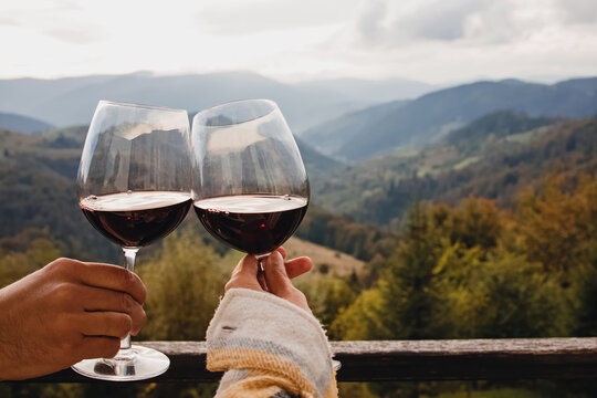 Man and woman clinking with glasses of red wine with a scenic mountain view.