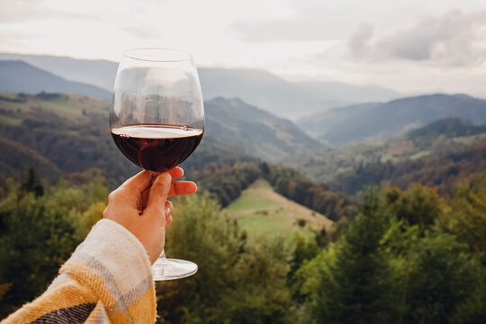 Woman's hand holding a glass of red wine with a mountain view.