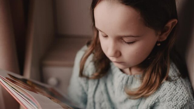 the young woman reads fairy tales by the window and flips through a book of childhood stories