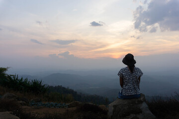 Asian women tourists sit and watch the beauty of the sunset, View of the mountains, misty clouds at dusk.