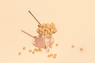 Martini glass with decorative golden balls and straw on pastel background. Festive and party concept. Minimal style.