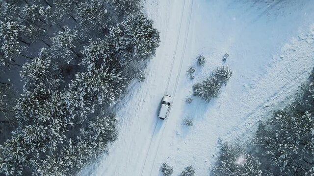 Aerial top view from drone of suv vehicle driving on snowy ice road exploring local landscapes in winter