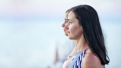 Side-view portraits of mother and teenage daughter against sea background. Two generations.