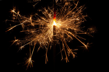 Horizontal conceptual close-up photo of an isolated 
sparkler in the process emitting a lot of bright sparks in the dark
