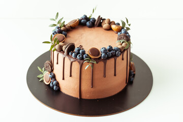 Chocolate cake decorated with blueberries, cookies and chocolates on a white background. Flat lay of the brown birthday cake