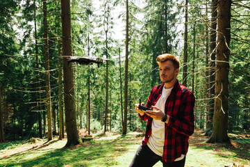 Young male operator controls a drone in a mountain forest with beautiful nature. Hiker flies a...