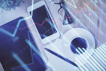 Double exposure of forex chart hologram over desktop with phone. Top view. Mobile trade platform concept.