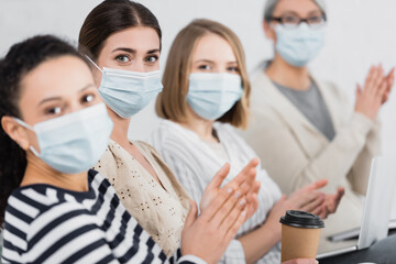 multicultural businesswomen in medical masks applauding during seminar