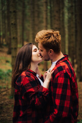 Love story photo, a couple in red shirts hugging and kissing on a hike. Beautiful couple in love in red shirts passionately kissing in a coniferous forest among the trunks of trees.