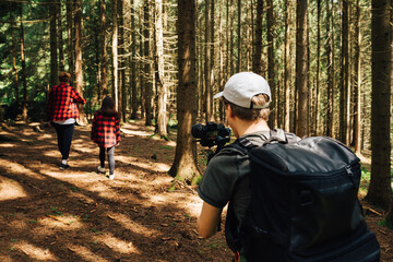 A young man shoots a camera with a stabilizer in love with a couple walking in the untouched forest on a sunny summer day. Video maker captures the love story of a couple in the woods on camera.