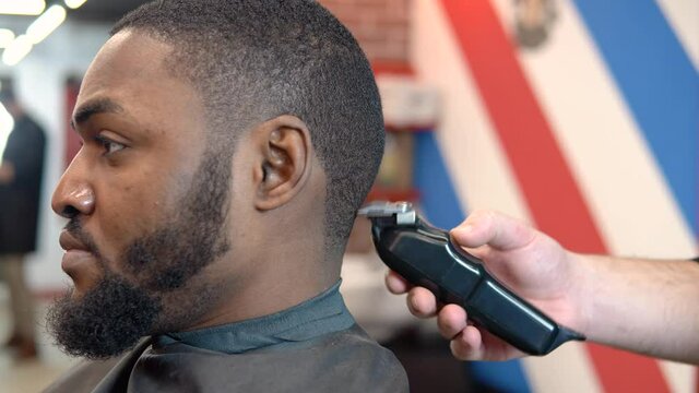 The hairdresser cuts the client's hair with a hair clipper