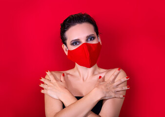 Woman with bright manicure dressed protective stylish red face mask and crossed hands on red studio background. Fashion new normal card. Surgical mask mockup