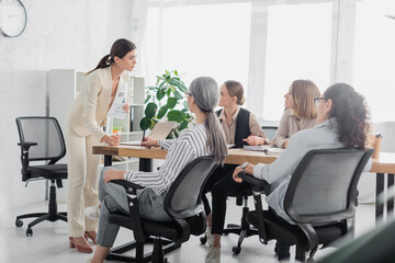 Fototapeta premium demanding team leader standing near multicultural businesswomen during meeting in office