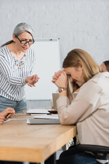 Obraz premium displeased asian team leader gesturing while talking with upset coworker in office