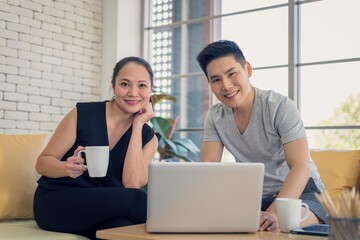 Asian man and woman family in casual outfit sitting in living room drinking coffee and using laptop together in happy and smile emotion