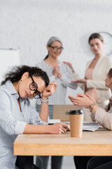 African american businesswoman sitting at desk near coworkers on blurred background