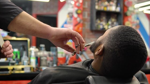 The hairdresser cuts with scissors and combs the client's beard with a comb. Beard care. Man's beauty