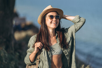 Pretty female traveler in hat and sunglasses with sea behind.