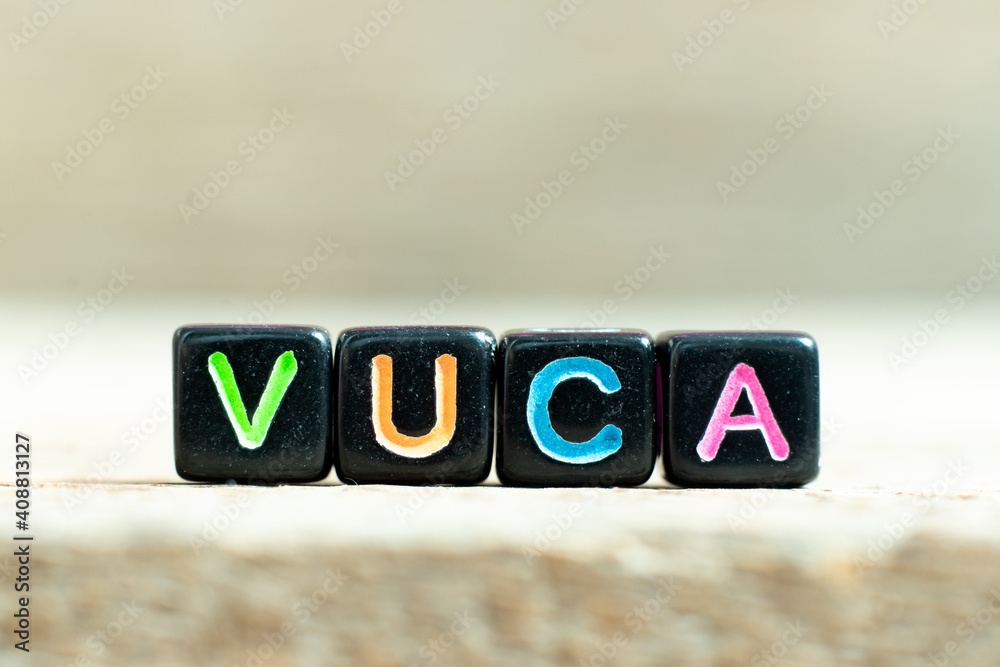 Poster Black color block with word VUCA (abbreviation of Volatility, uncertainty, complexity and ambiguity) on wood background