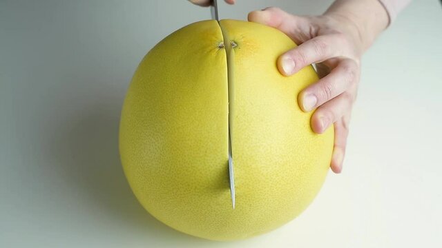 Female hands cutting in half a delicious large citrus fruit pomelo, close up.