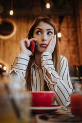 Beautiful young adult woman sitting in a nice restaurant or coffee bar and drinking fresh good coffee. She is alone and serious.