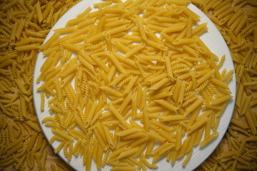 Pasta on a white round wooden tray on a wooden table. Top view. Macaroni is everywhere